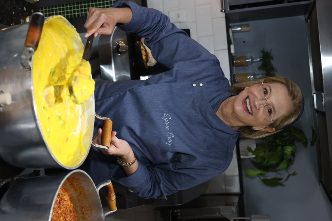Sylvia Cury tirando uma porção da panela para servir à mesa